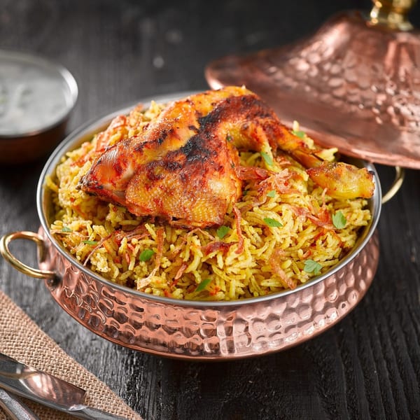 Chicken biryani in a hammered copper bowl with a matching lid and a side of raita.
