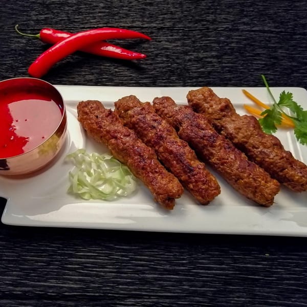 Five India Gate seekh kebabs with red sauce, shredded cabbage, and red chilies on a white plate.
