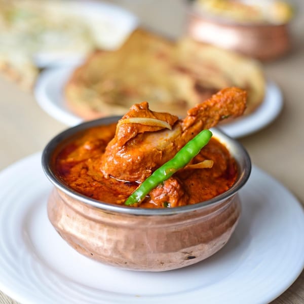 Chicken curry in a copper bowl, garnished with a green chili and onion slices.