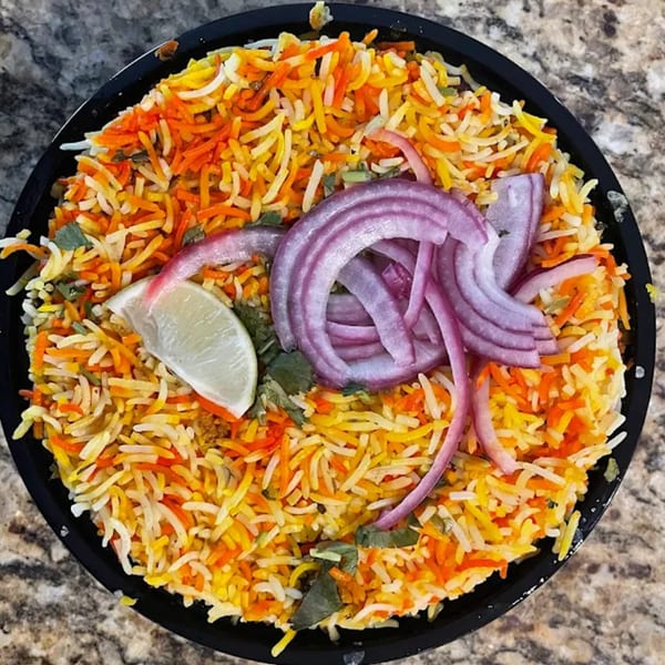 Colorful Indian biryani rice with red onions and a lime wedge in a black bowl.